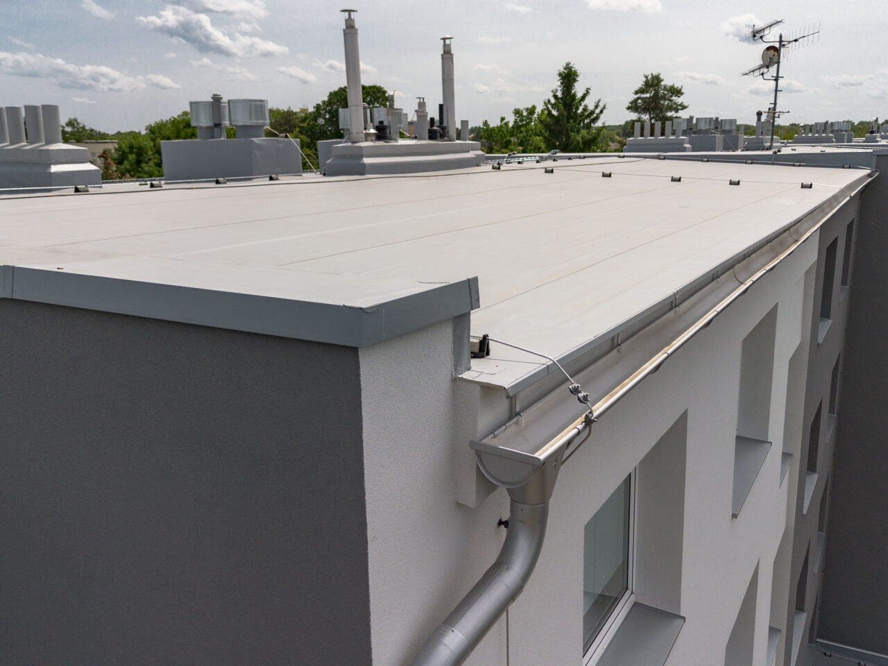 Pohled na zateplenou plochou střechu panelového domu s novým hromosvodem a okapem